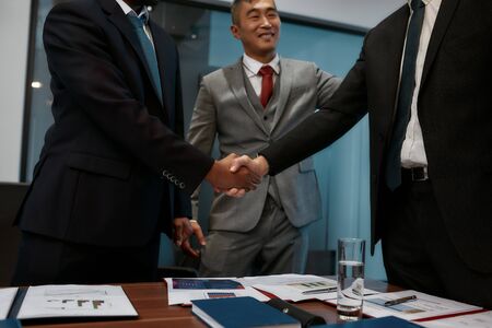 Deal. Two businessmen in classic wear shaking hands while having a meeting in the modern officeの写真素材
