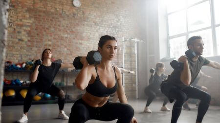 Play strong. Young athletic woman lifting dumbbell while having workout at industrial gym. Group training conceptの写真素材