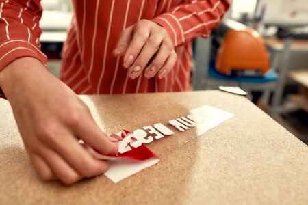 Cropped shot of woman removing the backing from advertisement sticker with text while preparing it to be printed on a T-Shirt. Printing on clothing and textiles concept. Horizontal shotの写真素材