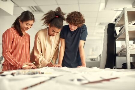 A simple place for dressmaking. Young cheerful designers working together in a studio. Group of creative millennials sharing and discussing ideasの写真素材