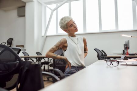 Killful pain. Young attractive tattooed businesswoman with short haircut suffering from back pain...