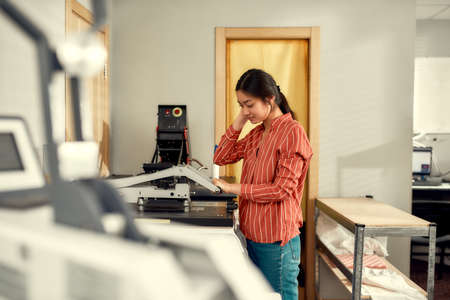 Quality printing. Young cheerful female worker using heat press transfer machine for printing...