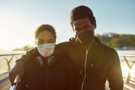 Keep yourself active during the quarantine. Young african couple wearing face medical mask while running together on the bridge in the morningの写真素材