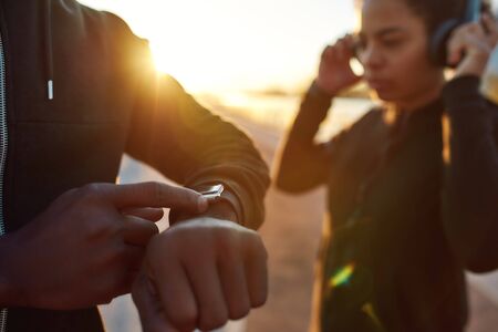 Close up of african male runner touching smartwatch, fitness app, getting ready to run in the early morning. Cropped photoの写真素材