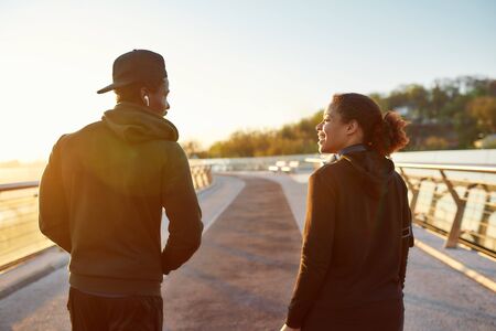 Running on the bridge at sunrise. African couple talking before morning jog outdoors. Female and male adult african athletes. Back viewの写真素材