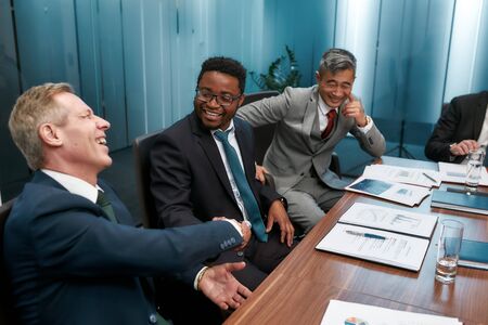 Deal of the day. Happy multicultural business people in classic wear shaking hands and smiling while having a meeting in the modern officeの写真素材