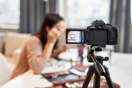 Bringing imagination to real life. Asian female blogger showing her makeup techniques and secrets while recording a tutorial video for her beauty blog using camera at homeの写真素材