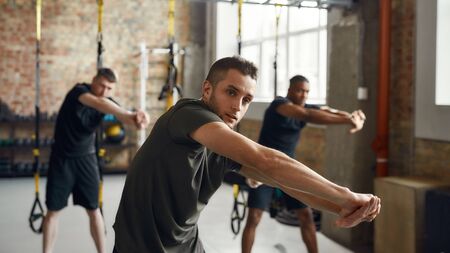 Make yourself stronger than your excuses. Portrait of diverse athletic men stretching body while working out together in industrial gym. Group training conceptの写真素材