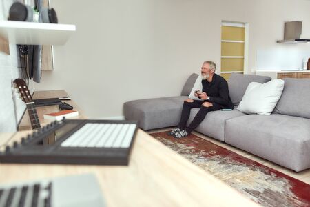 Gamer. Bearded middle-aged man, artist holding controller, playing video games, sitting on the couch at home. Weed vaporizer, dry herb vape pen lying next to himの写真素材