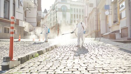 Diligence. Sanitization, cleaning and disinfection of the streets and alleys in the city center due to the emergence of the Covid19 virus. Specialized team in protective suits and masks at workの写真素材