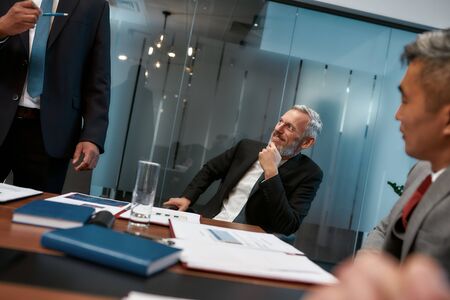 Working with pleasure. Happy mature businessman in formal wear listening to his colleague and smiling while having a meeting in the modern officeの写真素材