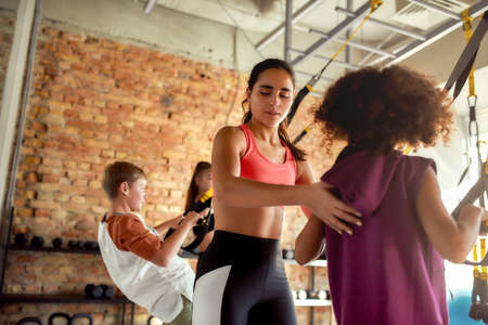 Explaining kids how to do it. Portrait of female trainer helping teenage girl while she is training using fitness straps in gym. Sport, healthy lifestyle, physical education conceptの写真素材