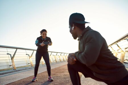 Smile. Happy african man stretching on the bridge and smiling while his girlfriend taking photo of...
