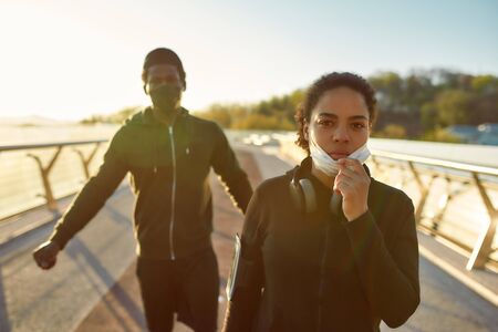 Keep Distance. Young african couple wearing face medical masks while running together on the bridge in the morning. Covid-19の写真素材