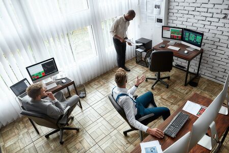 A world of business. High-angle view of three traders having chat while sitting by desks in front of...