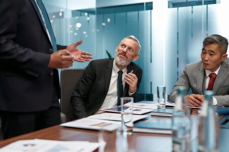 Portrait of smiling mature businessman in formal wear sitting at the office table while having a meeting in the modern officeの写真素材