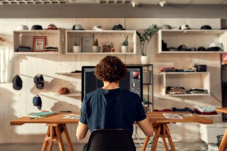 Excellence in graphic. Portrait of male worker sitting by desk, drawing sketches logo design using pc. Young man working at custom T-shirt, clothing printing companyの写真素材