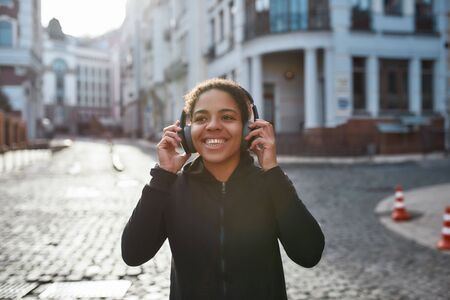 Morning jog with music. Happy african female runner wearing headphones looking at camera and...