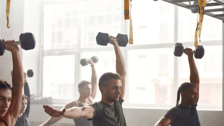 Health is a priority. Group of sportive people lifting dumbbell while having workout at industrial gym. Group training, teamwork conceptの写真素材