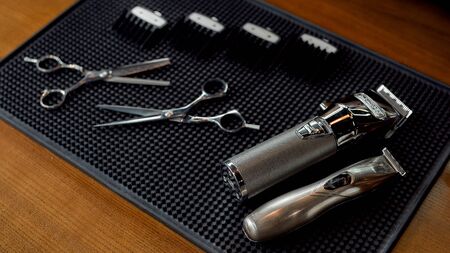 Scissors, electric hair trimmers and four different nozzles lying on a rubber mat in the barbershop. Professional barber tool kitの写真素材