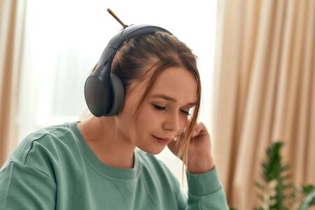 Happy beautiful woman in headphones with closed eyes listening music or studying language online,...