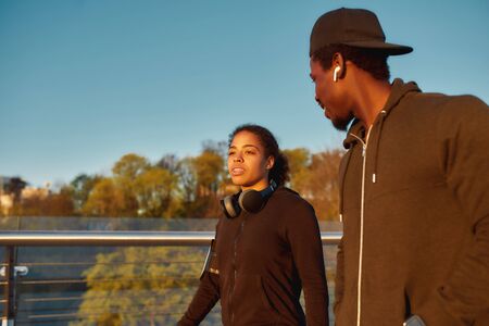 Jogging with partner. Young african female athlet talking with her boyfriend before morning jog. African sporty couple running together at sunriseの写真素材