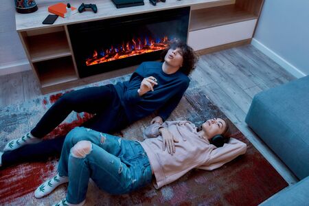Young teenage couple smoking marijuana and relaxing together while lying on the floor at home. Guy smoking cannabis weed cigarette. Girl listening musicの写真素材