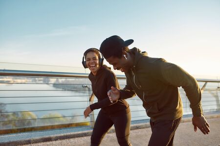 Enjoying run. Side view of happy young African couple, man and woman in headphones laughing while...