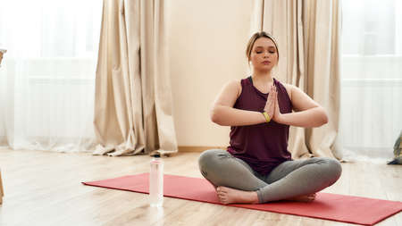 For your harmony. Young curvy woman in sportswear meditating sitting in the lotus position on a yoga mat at homeの写真素材