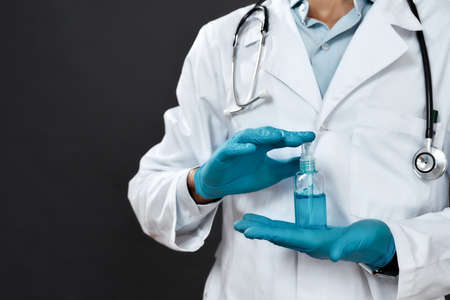 Cropped photo of male doctor in medical uniform with stethoscope around neck holding antiseptic gel...