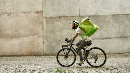 Turbo food, Turbo speed. Bearded delivery man in helmet with thermo bag or backpack riding a bike along the city, delivering food. Courier, delivery service conceptの写真素材
