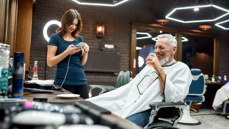 Barbershop is not just a haircut. Handsome middle-aged man drinking something and having fun while...