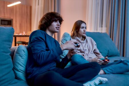 Young beautiful couple or friends playing video games while sitting on the couch at home. Young...