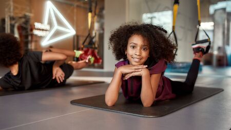 Teenage girl smiling at camera while doing exercises on mat using fitness straps in gym. Sport, healthy lifestyle, physical education conceptの写真素材