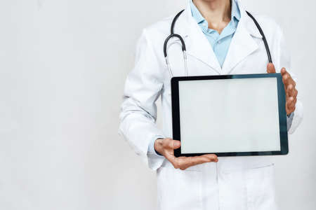 Cropped shot of a doctor in medical uniform showing digital tablet at camera while standing against grey backgroundの写真素材