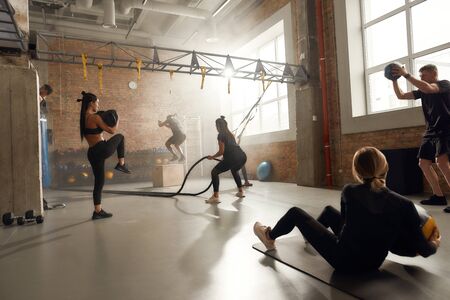 Squat. Jump. Throw. Lift. Full length shot of sportive people having workout at industrial gym. Group training, teamwork conceptの写真素材