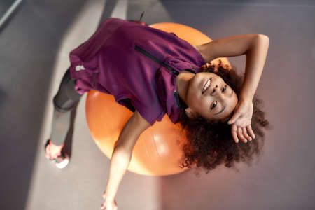 African american teenage girl smiling at camera while working out with exercise ball in gym. Sport,...