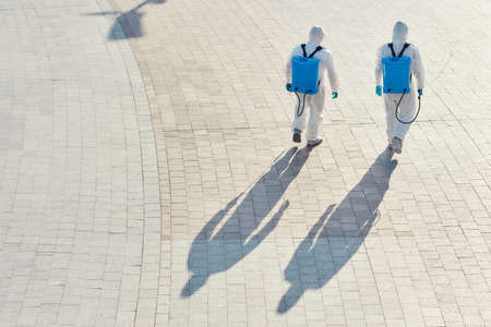 Making the city clean. Sanitization, cleaning and disinfection of the city due to the emergence of the Covid19 virus. Specialized team in protective suits and masks walking outdoorsの写真素材