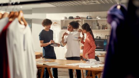 When quality really matters. Creative people trying on stickers with text, while discussing logo and design of T-shirt. Young man and women working at custom T-shirt, clothing printing companyの写真素材