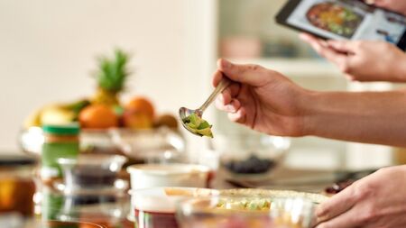 Close up of process of cooking. Man preparing meal while woman checking recipe using tablet. Vegetarians cooking in the kitchen together. Vegetarianism, healthy food, diet, stay home conceptの写真素材