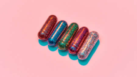 Creative concept with colorful glitter pills isolated on pastel pink background. Minimal style, art conceptの写真素材