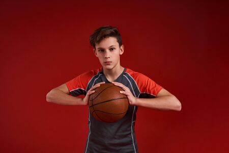 Winners never quit and quitters never win. A teenage boy engaged in sport, looking at camera and holding basketball. Isolated on red background. Training, active lifestyle concept. Horizontal shot.の写真素材