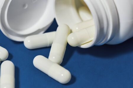 White pills, capsules scattered from a white bottle, jar on a blue backgroundの写真素材