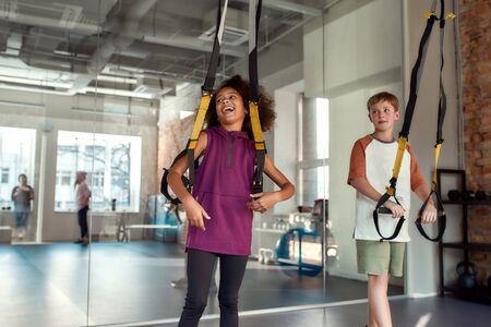 Portrait of teenage girl having fun while training with other kids using fitness straps in gym. Sport, healthy lifestyle, physical education conceptの写真素材