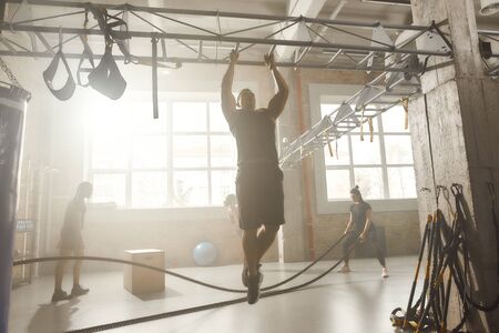 The health club. Full length shot of athletic man doing pull ups on the bar while having workout at...
