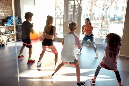 Kids working out using resistance band in gym together with female trainer. Sport, healthy lifestyle, physical education conceptの写真素材
