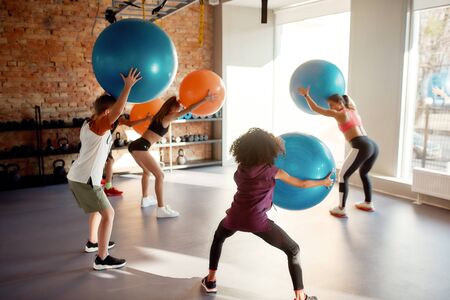 Teenagers having fun while working out with female trainer using exercise ball in gym. Focus on kids. Sport, healthy lifestyle, physical education concept. Horizontal shotの写真素材