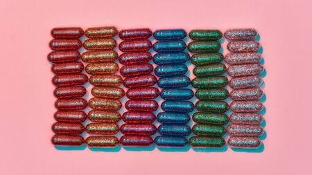 Creative concept with many colorful glitter pills lying in rows isolated on pastel pink background....