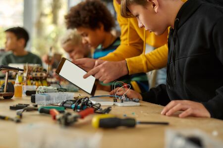 Sharing ideas. Cropped shot of young technicians working with a wiring kit at a stem robotics class. Male teacher is helping them, giving advice, using tablet pc. Inventions and creativity for kidsの写真素材
