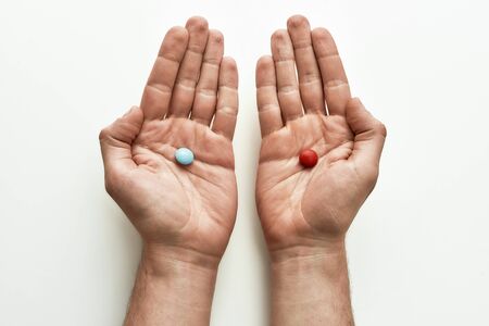 Top view of blue pill in one hand and red pill in another over white background. Concept of choice and treatment. Selective focus. Horizontal shotの写真素材